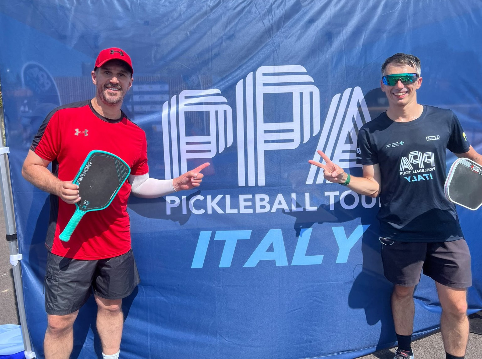 Dwóch zawodników z rakietkami na tle baneru PPA Pickleball Tour Italy
